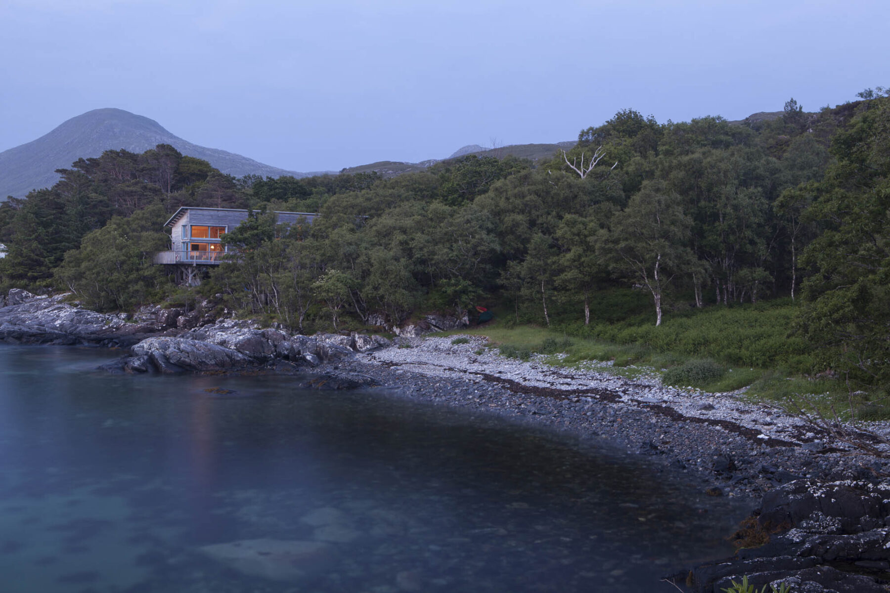 Timber house 'Frisealach' sitting amongst trees above the shoreline. Roshven, west coast of Scotland.